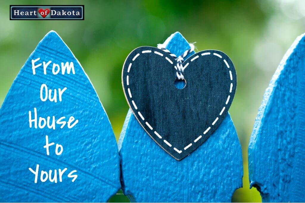 Blue painted wooden fence with a navy blue heart hung around the center post. White text to the left reads "From Our House to Yours."