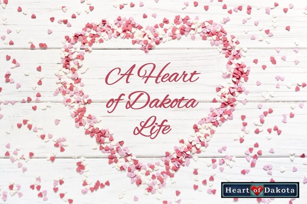A Heart of Dakota Life - photo a heart outline made out of rose petals on white wood backdrop. In the center of the heart, red decorative text reads "A Heart of Dakota Life."