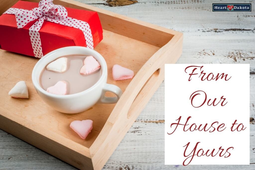 Heart of Dakota From Our House to Yours - photo of a wooden tray. On the tray sits a rectangular gift box wrapped in red. To its right sits a white ceramic mug filled with hot chocolate. Floating in the beverage are heart-shaped marshmallows.
