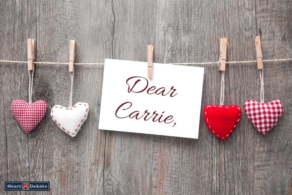 White paper note hanging to a twine clothesline, along with 4 miniature cloth hearts. Decorative text on the note reads: "Dear Carrie."
