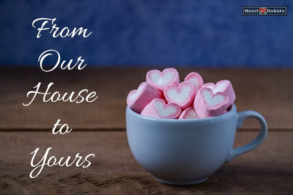 White mug filled with pink and white heart-shaped marshmallows. White text to the right reads: "From Our House to Yours."