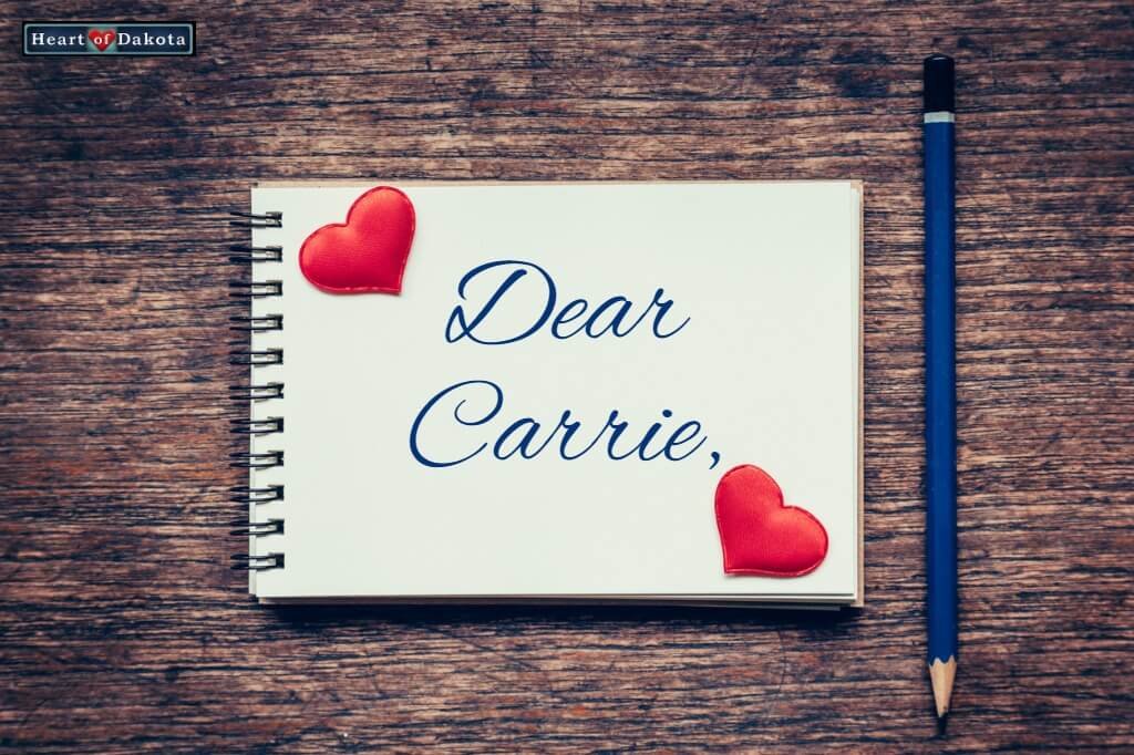 White spiral-bound notebook page with "Dear Carrie" written on it in blue decorative script.